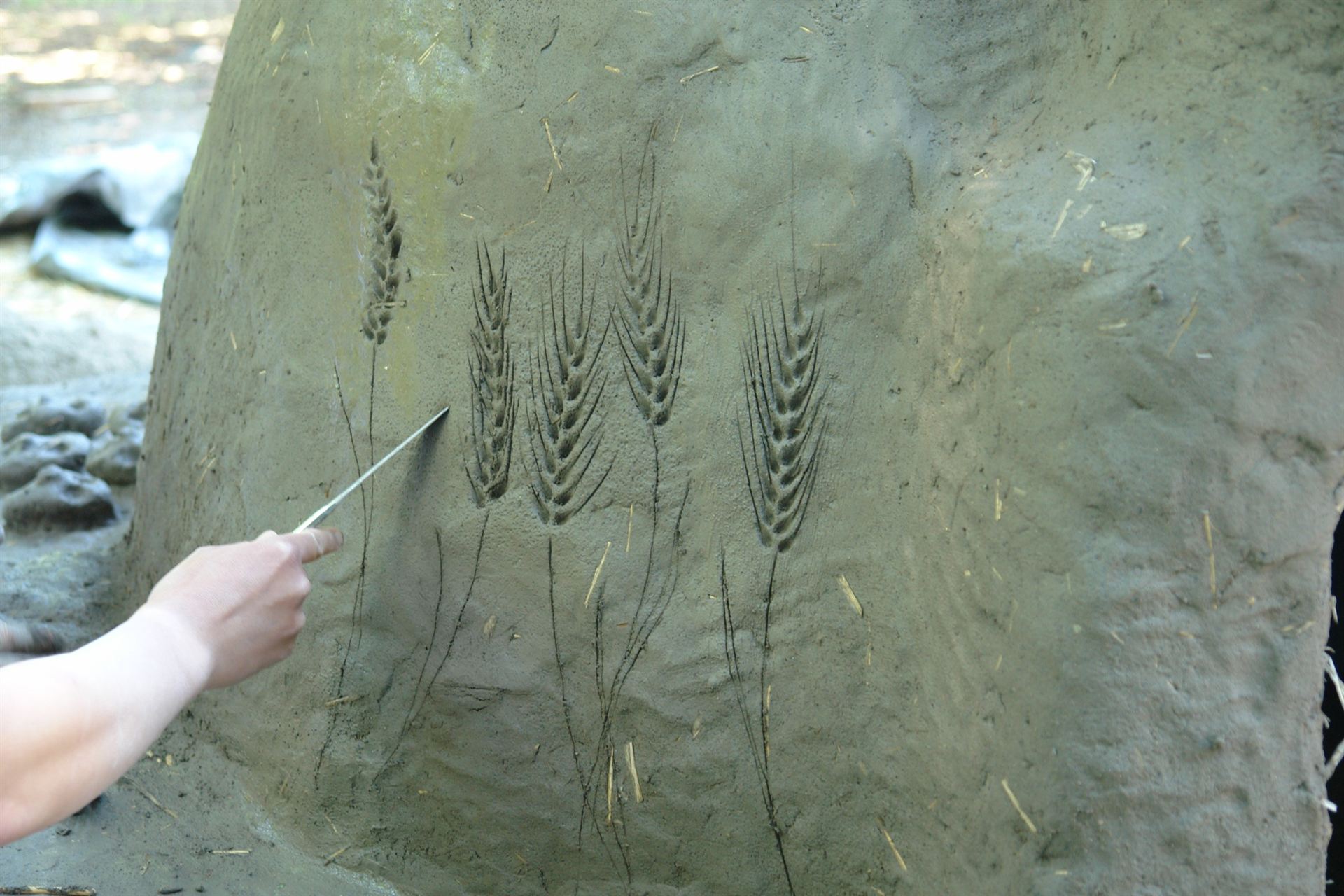 Hands shaping a design into a cob oven made of earth and straw